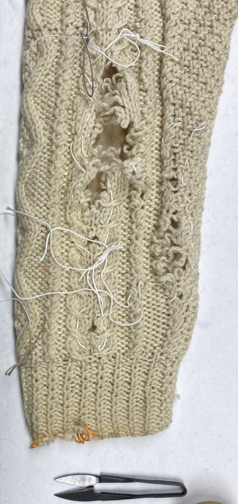 large raveled hole in an oatmeal colored knitted sleeve