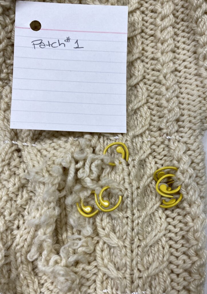 A large hole in one sleeve with yellow split stitch markers showing smaller breaks in the yarn