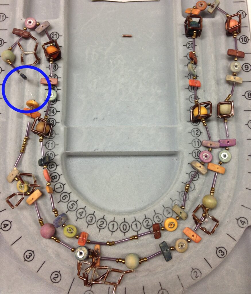 necklace of assorted shapes and colors of beads on a broken monofilament line with a circle highlighting the break